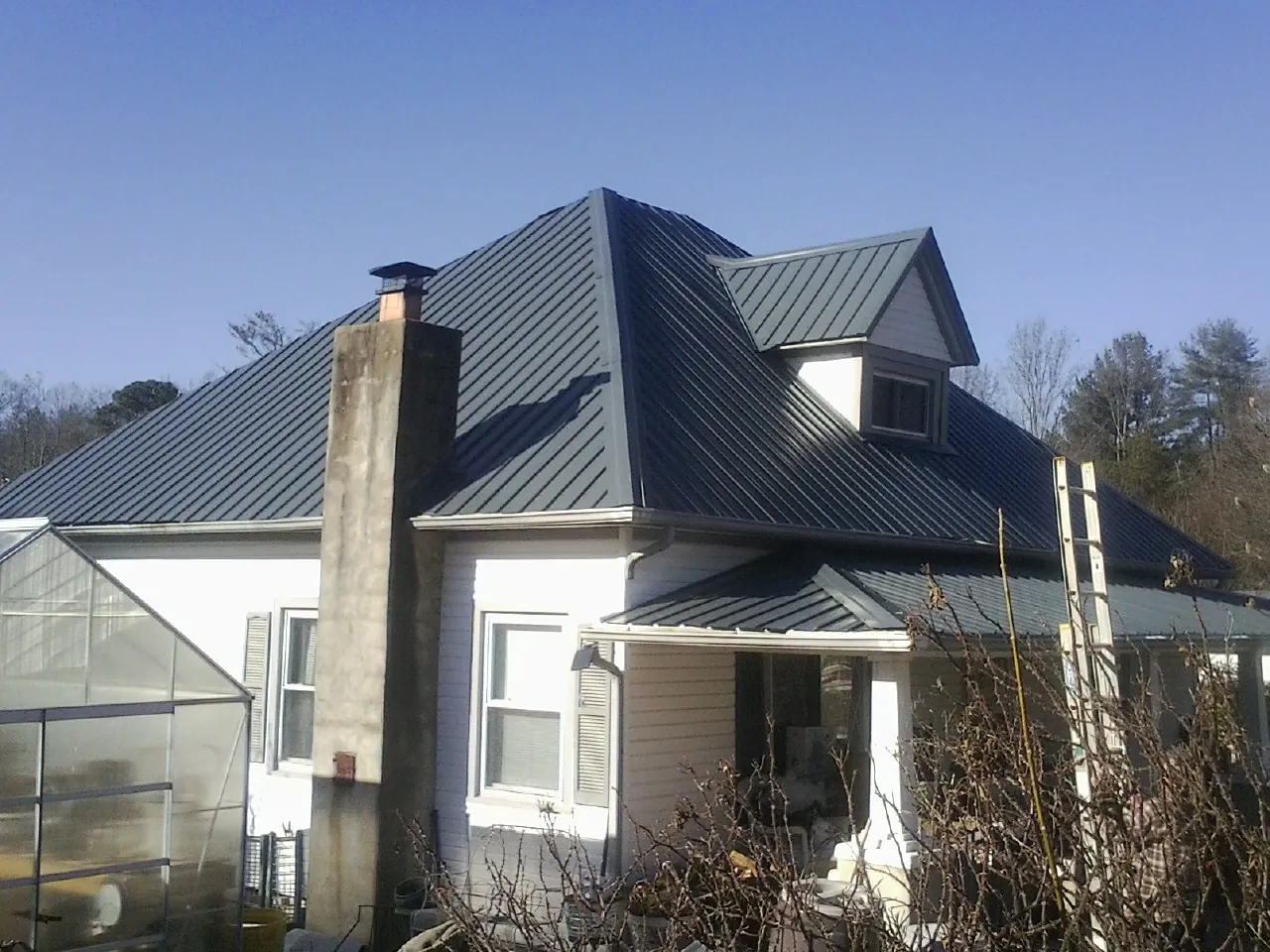 Dark blue standing seam metal roof on a white farmhouse with dormer — Slate & Tile Roof Repair by Roofing Brothers in Stockport