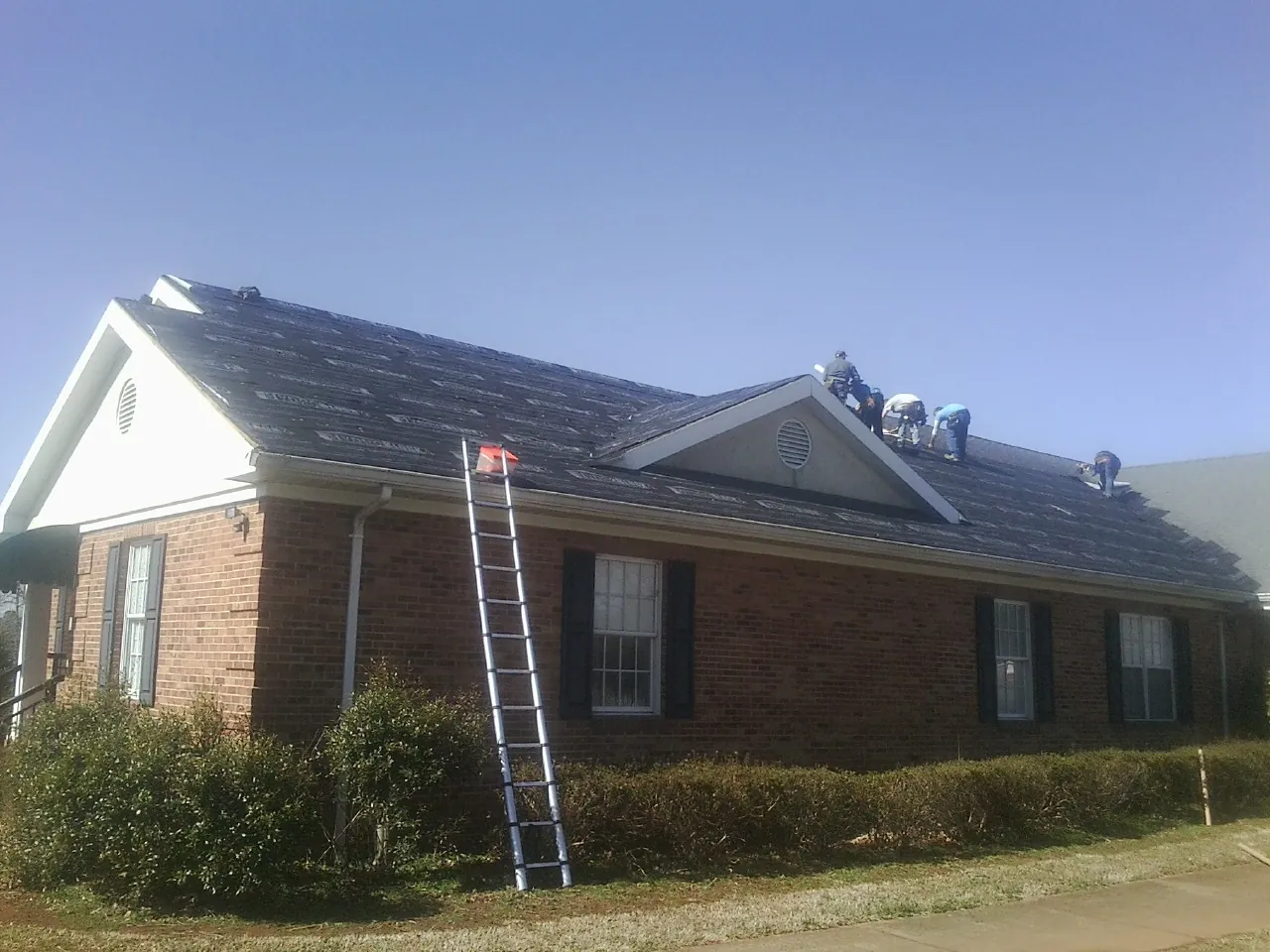 Crew tearing shingles off a brick ranch roof with a ladder set — Metal Roof Repair work by our crew in Stockport