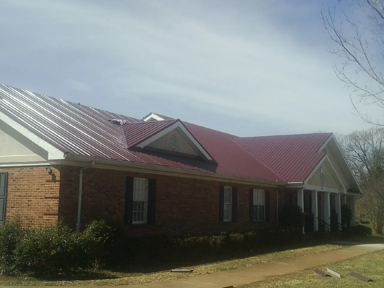 Red metal roof with gabled entries on a long brick building, from a Hail Damage Roof Repair job in Stockport