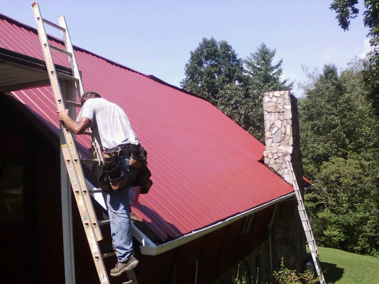 Roofer on a ladder beside a red metal roof and stone chimney in Stockport