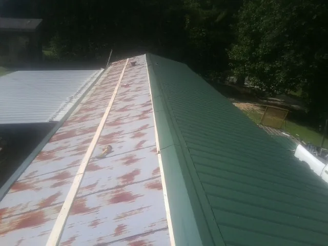 Old rusted panels beside newly installed green metal roofing — Wind Damage Roof Repair by Roofing Brothers in Stockport
