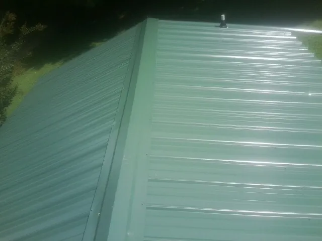 New green metal panels meeting at the ridge of a roof — Flat Roof Repair work by our crew in Stockport