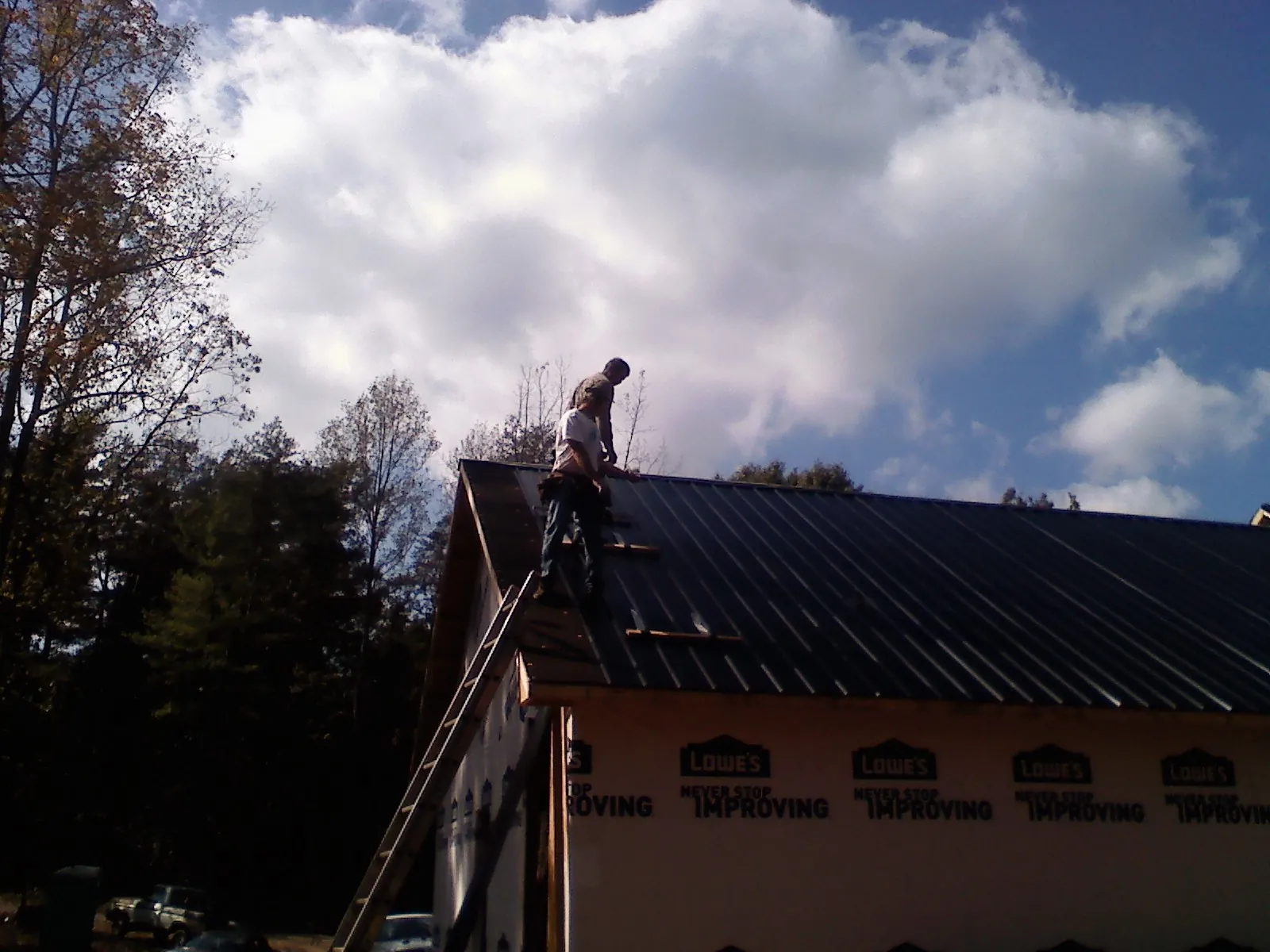 Roofer fastening dark metal panels high against a cloudy sky, from a Roof Inspection job in Stockport