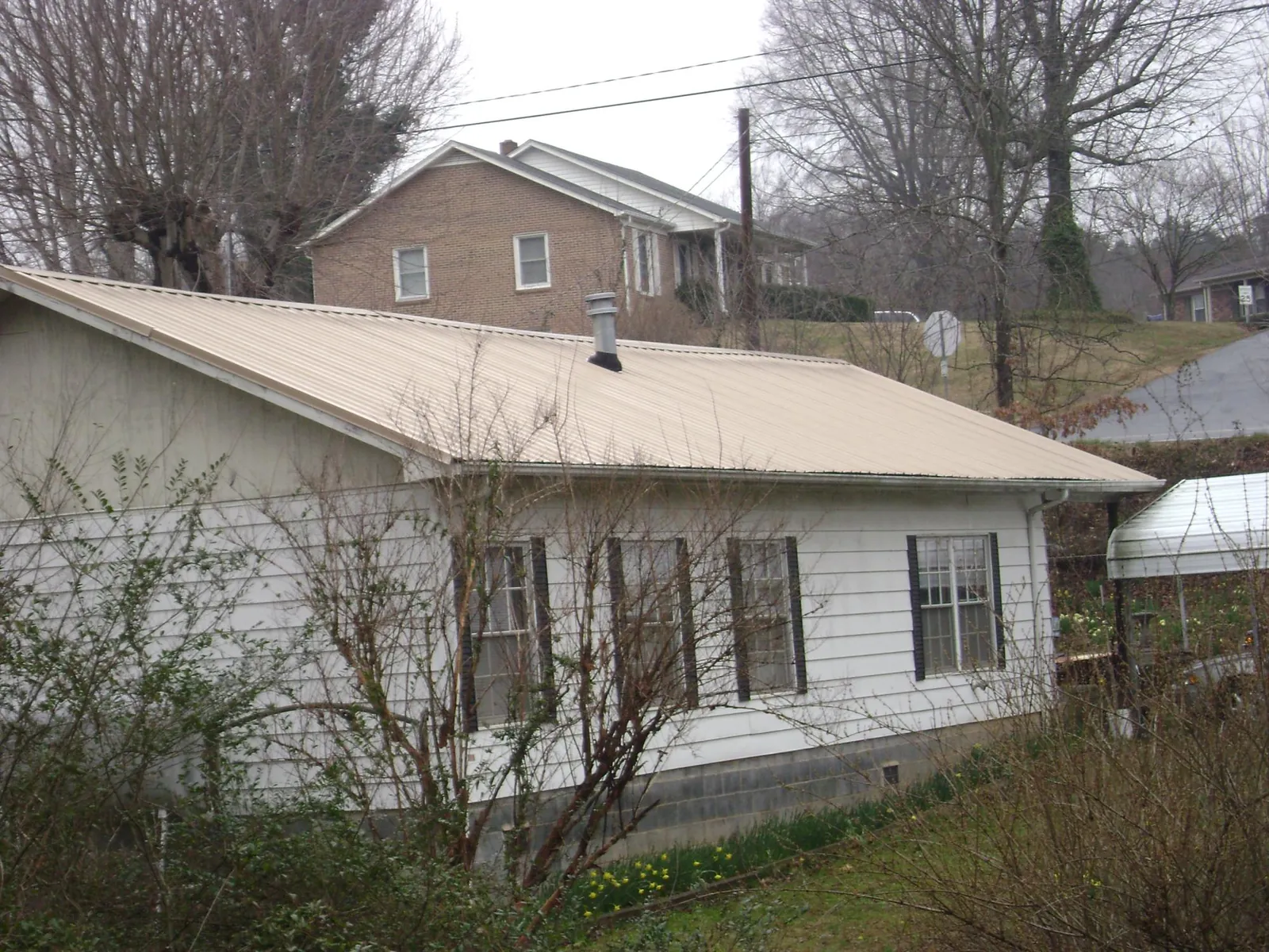 Tan metal roof on a white sided house set into a hillside — Commercial Roofing by Roofing Brothers in Stockport